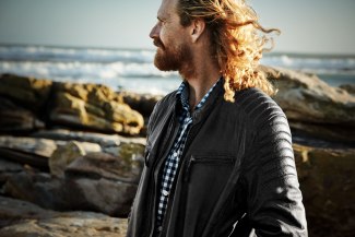 man with long hair standing in the wind close to the ocean